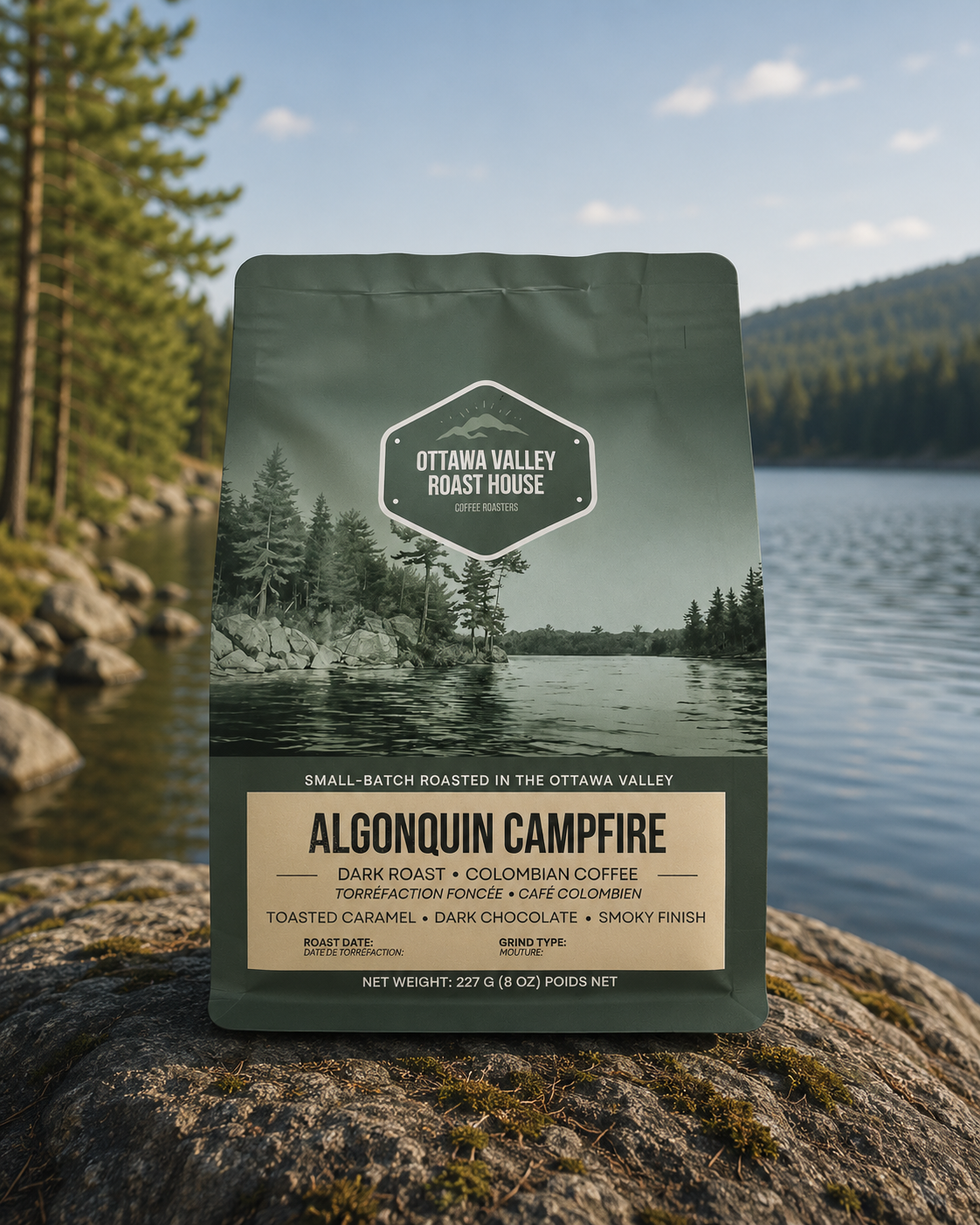A bag of Ottawa Valley Roast House Algonquin Campfire coffee stands on a rock by a lake, with a forested mountain and blue sky in the background.