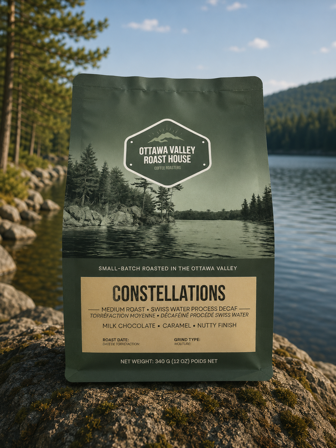 A stand-up pouch of Ottawa Valley Roast House Constellations coffee sits on a large rock outdoors with a lake, trees, and mountains in the background. The package is dark olive green with a scenic lake-and-trees photo and a beige label panel.