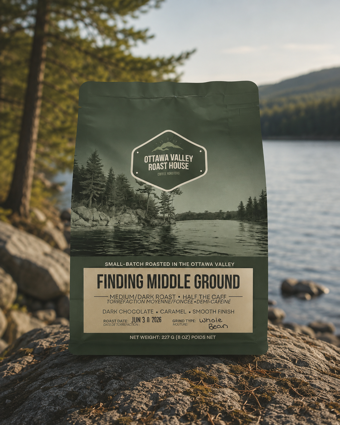 A bag of Ottawa Valley Roast House 'Finding Middle Ground' coffee stands upright on a rock with a blurred lake and forest background.