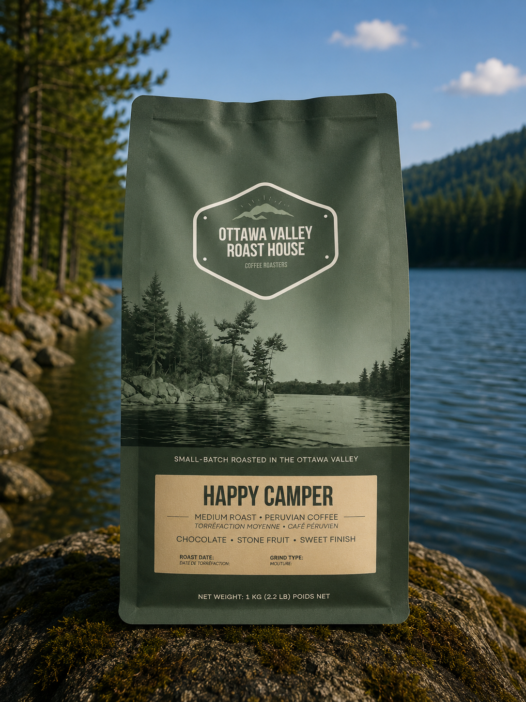 A stand-up pouch of Ottava Valley Roast House Happy Camper coffee is photographed outdoors on a mossy rock with a lake and forest in the background. The pouch is dark olive green with a scenic forest-and-lake label and a beige lower panel reading 'Happy Camper'.
