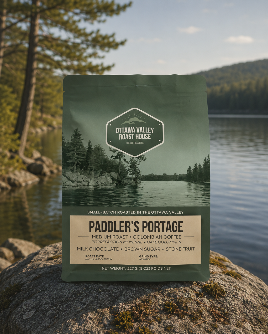 A stand-up coffee bag from Ottawa Valley Roast House labeled Paddler's Portage, placed on a large rock in front of a lake with trees and hills in the background.