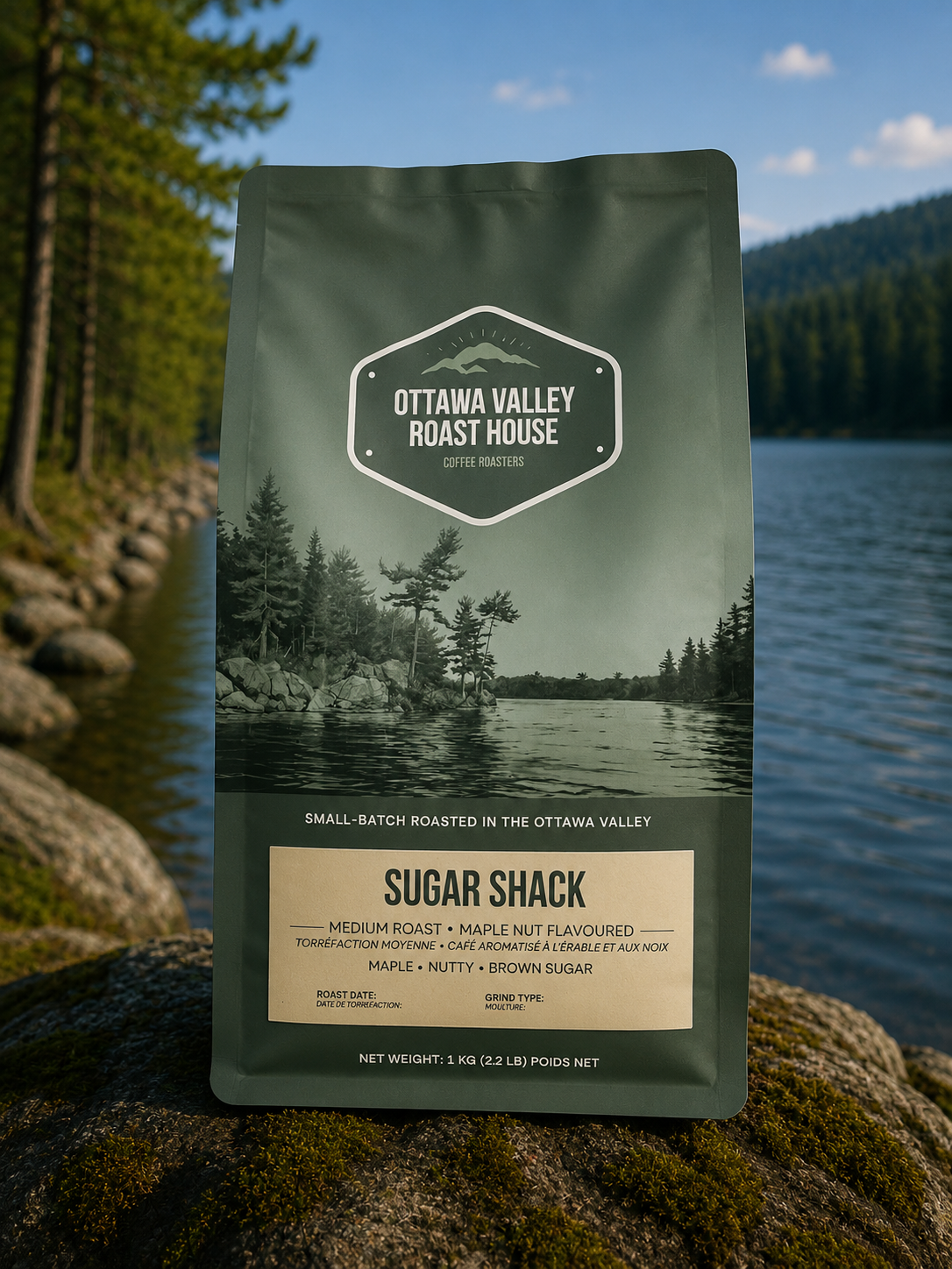 A stand-up pouch of Ottawa Valley Roast House Sugar Shack coffee stands on a mossy log by a lake, with forest trees and blue water in the background.
