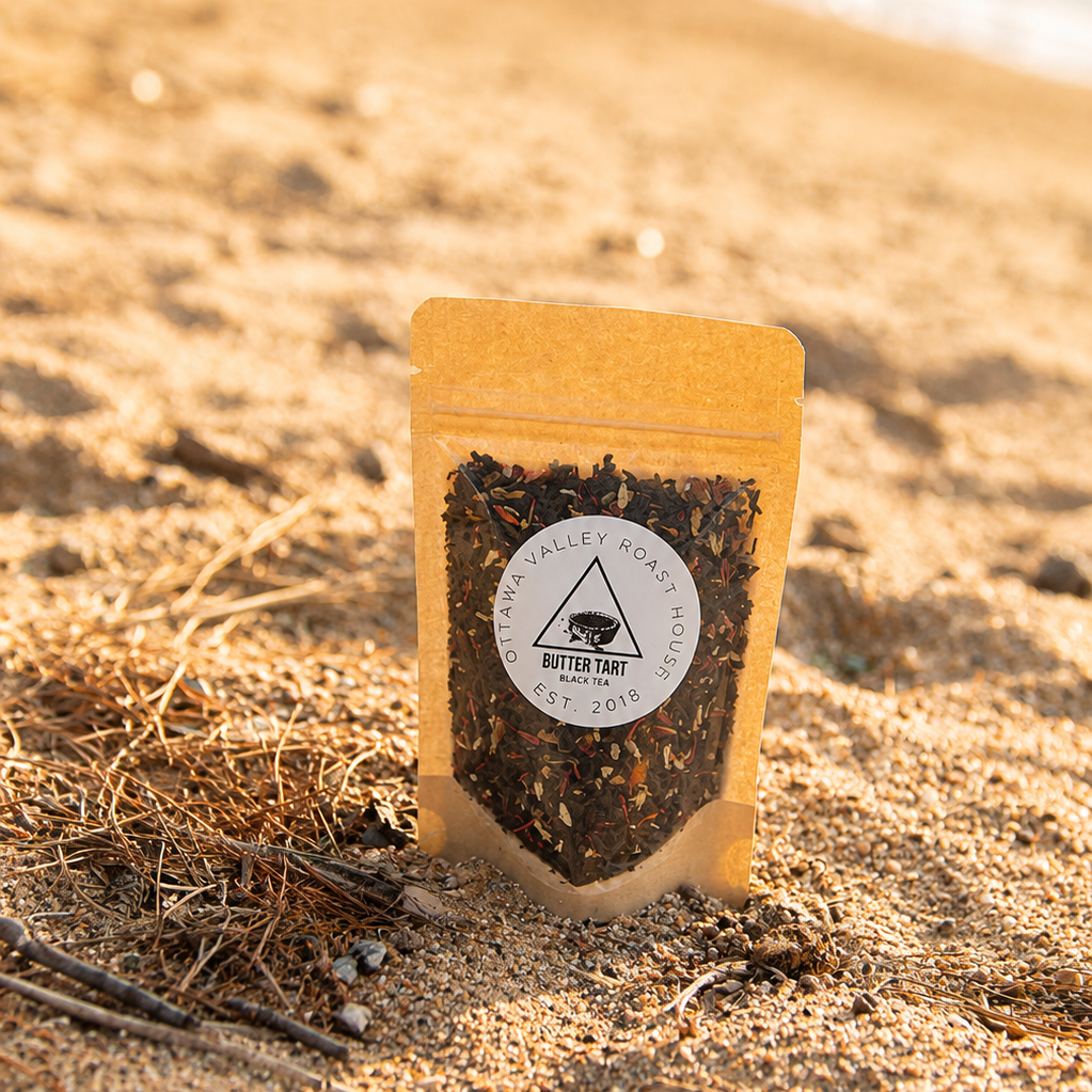 A stand-up pouch of Mitter Cut loose leaf tea set in a sandy beach environment with the ocean waves blurred in the background.