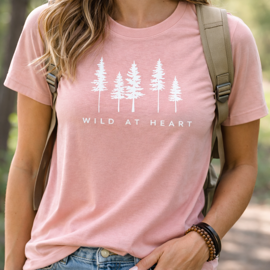 Person wearing a pink t-shirt with 'Wild at Heart' and tree design outdoors.