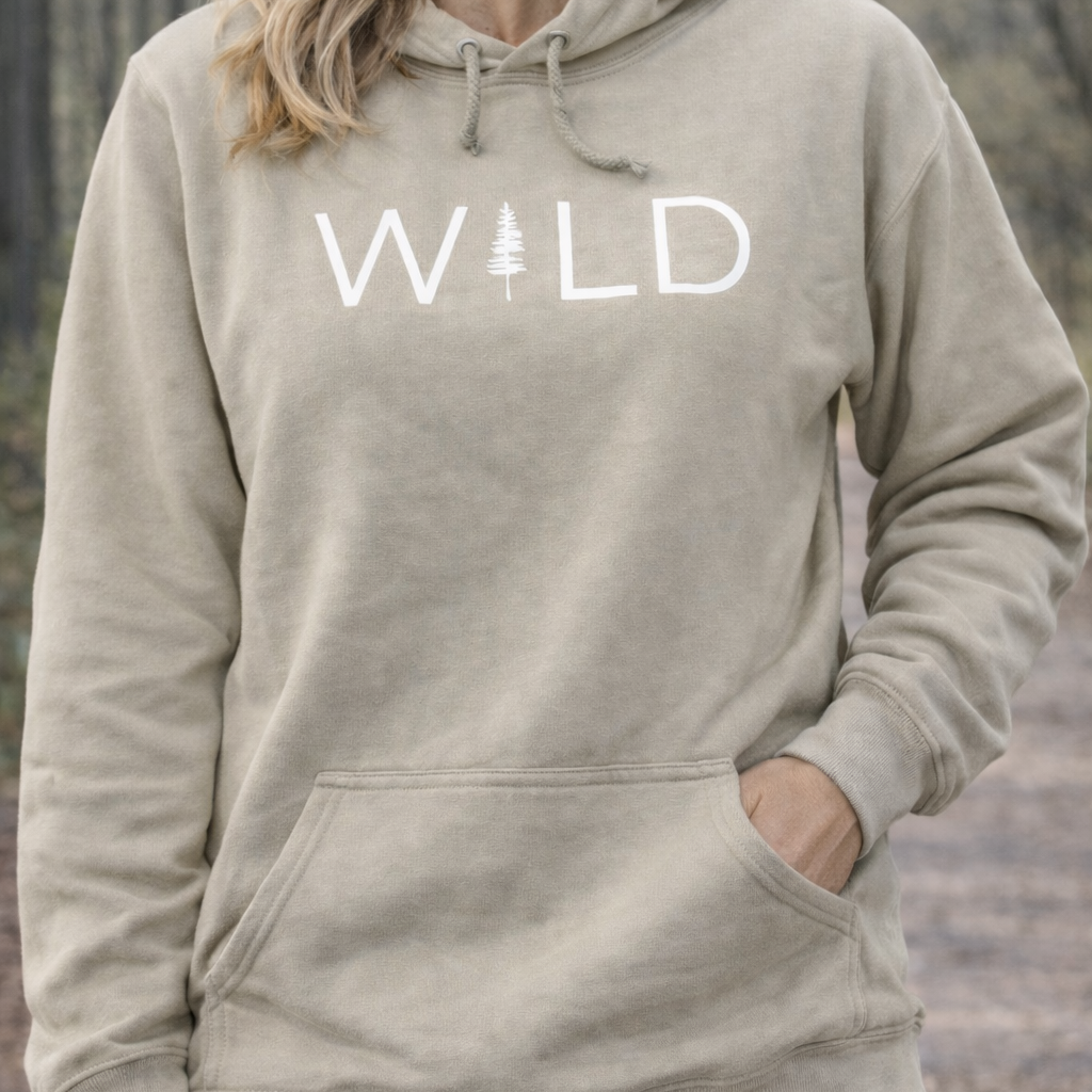 Person wearing a beige hoodie with 'WILD' printed on it against a blurred natural background