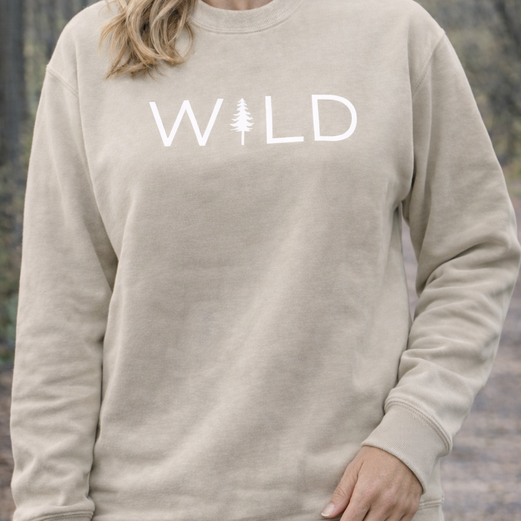 Beige sweatshirt with 'WILD' printed on it against a blurred natural background