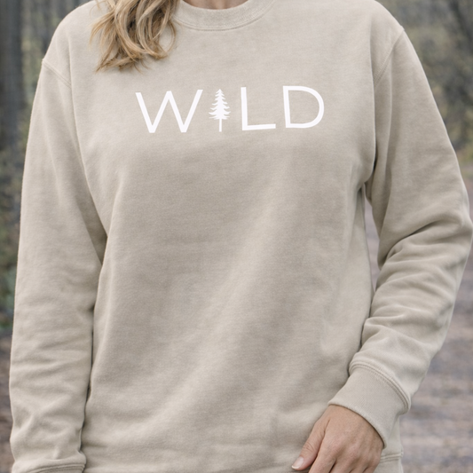 Beige sweatshirt with 'WILD' printed on it against a blurred natural background